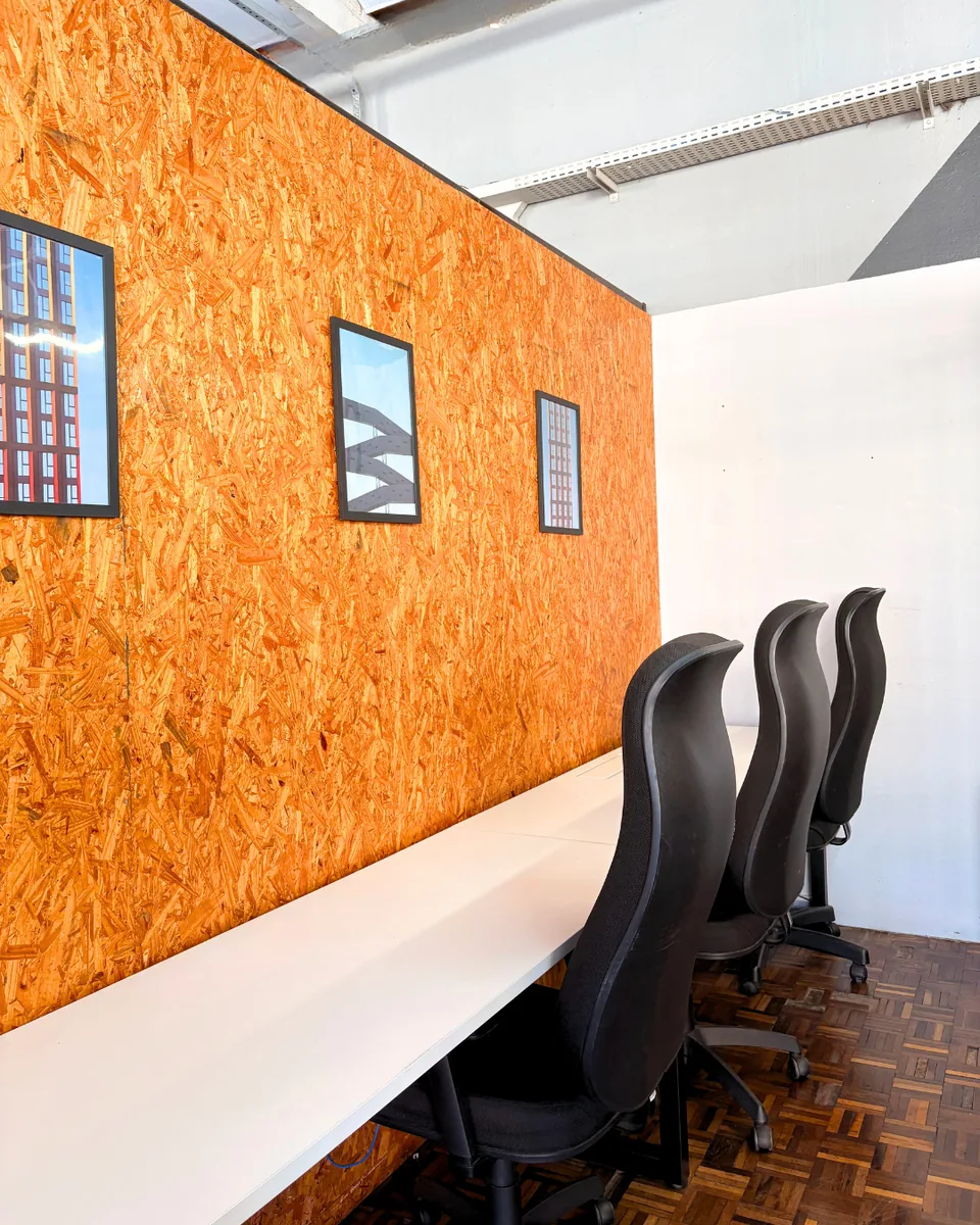 Sala privativa com bancada, cadeiras e parede laranja na Aldeia Coworking