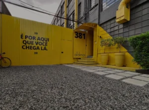 Entrada da Aldeia Coworking no Centro Cívico em Curitiba, com fachada amarela e frase motivacional.