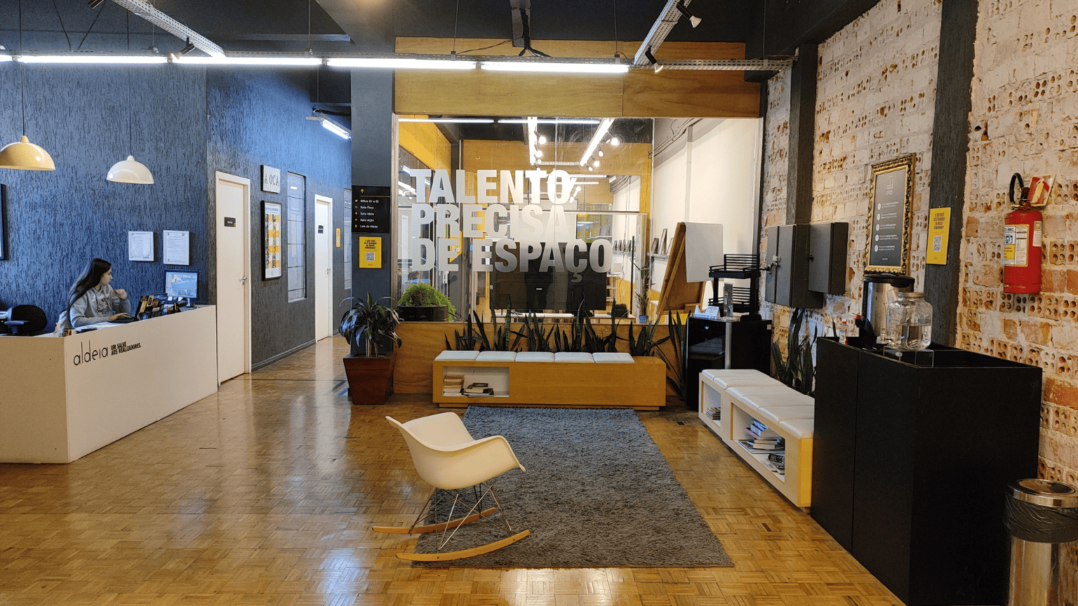 Recepção moderna da Aldeia Coworking Cândido, com ambientes aconchegantes, decoração industrial e espaço colaborativo para talentos criativos.